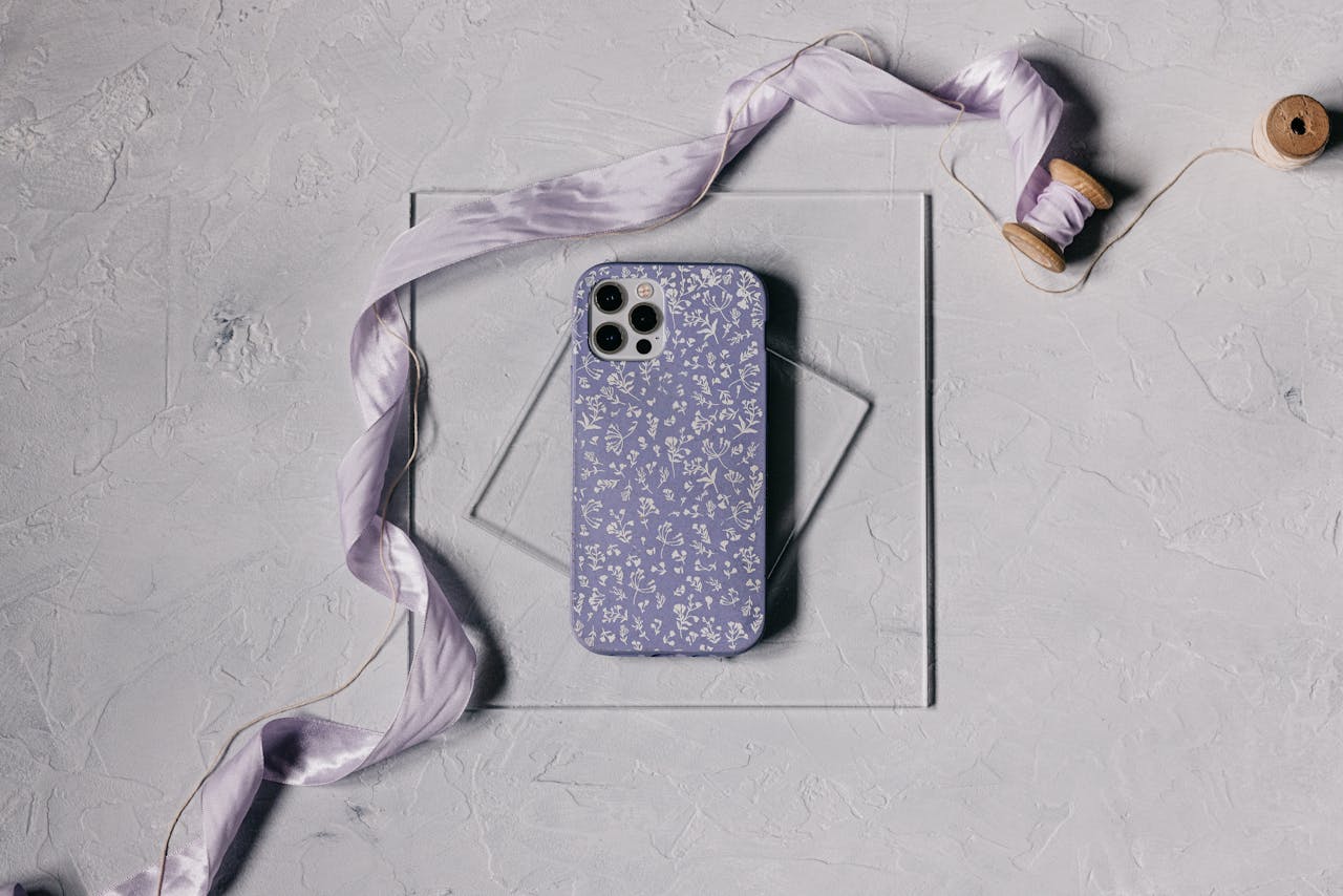 Artistic flat lay of a smartphone with a delicate floral case and lavender ribbon on a textured surface.